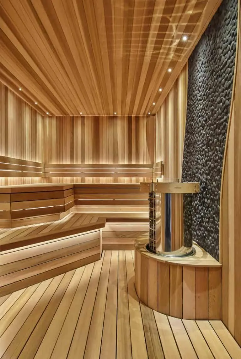 Helle Holzsauna mit Wand aus dunklen Kieselsteinen und rundem Edelstahlofen