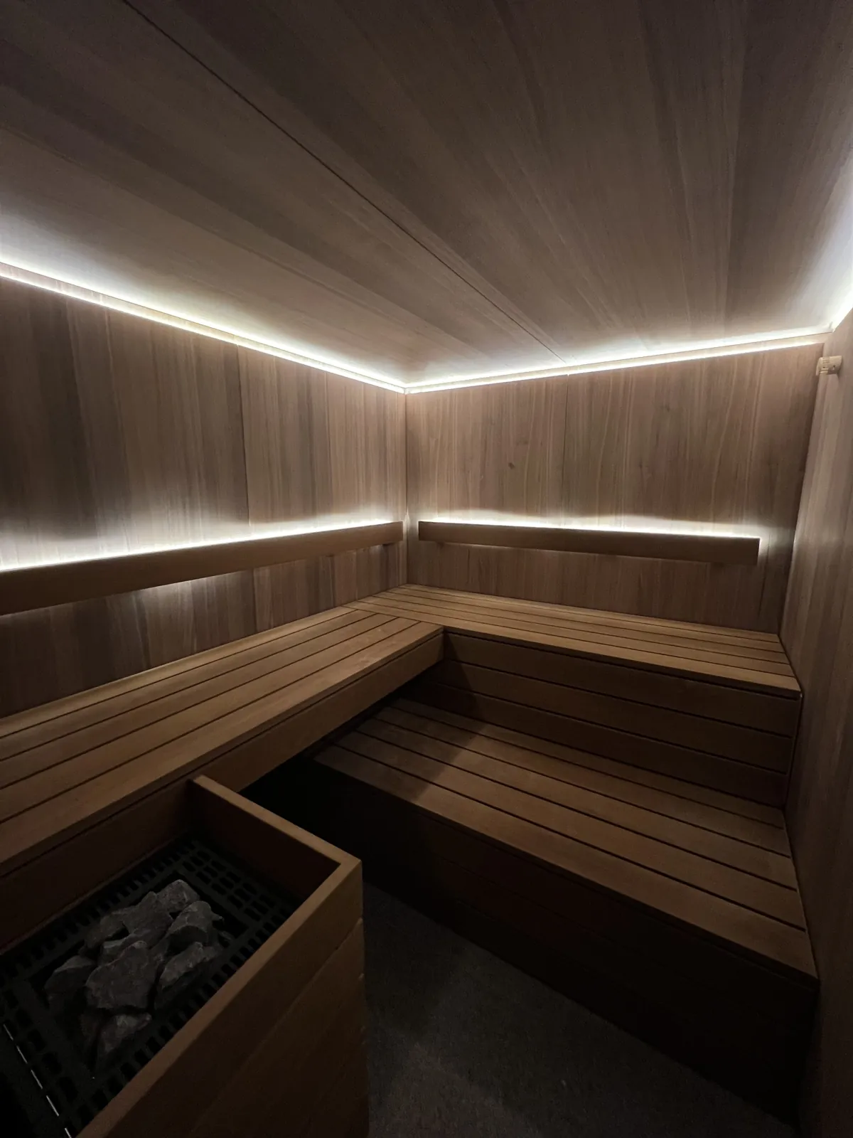Dunkle Holzsauna mit hellen Lichtbändern unter der Decke und hinter der Rückenlehne