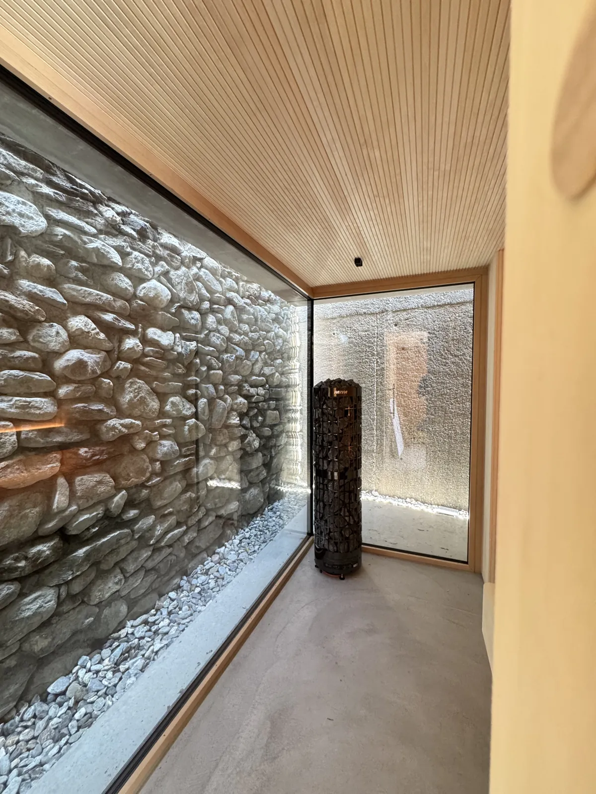 Sauna mit raumhoher Glasfront und Blick auf eine Natursteinmauer, Harvia-Säulenofen