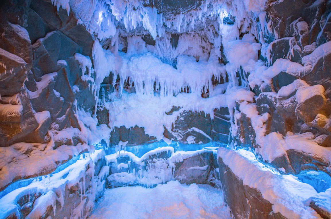 Schneeraum als Eisgrotte mit Felswänden, Eiszapfen und blau beleuchteten Sitzflächen