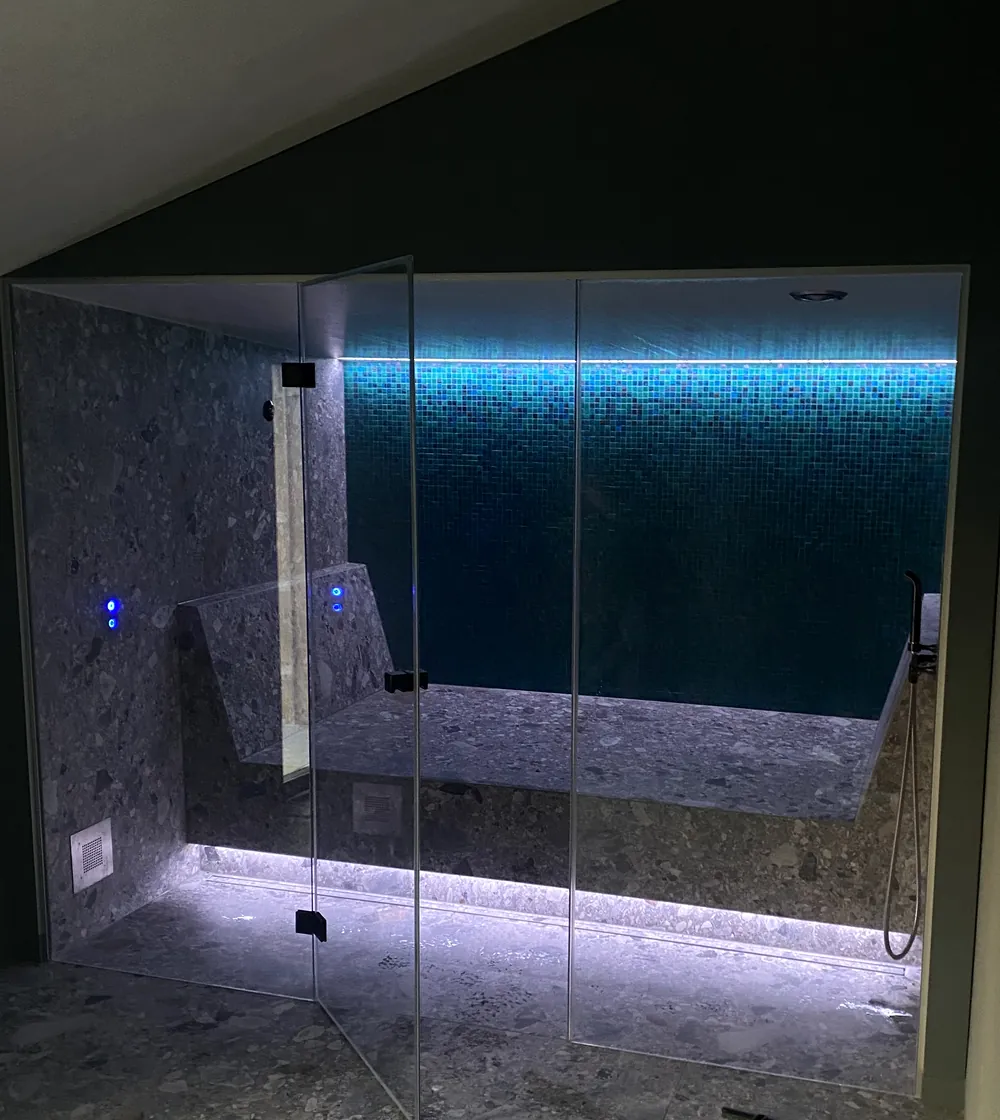 Dampfbad in Liechtenstein unter der Dachschräge mit Glasfront, Terrazzo-Sitzbank und türkisem Glasmosaik