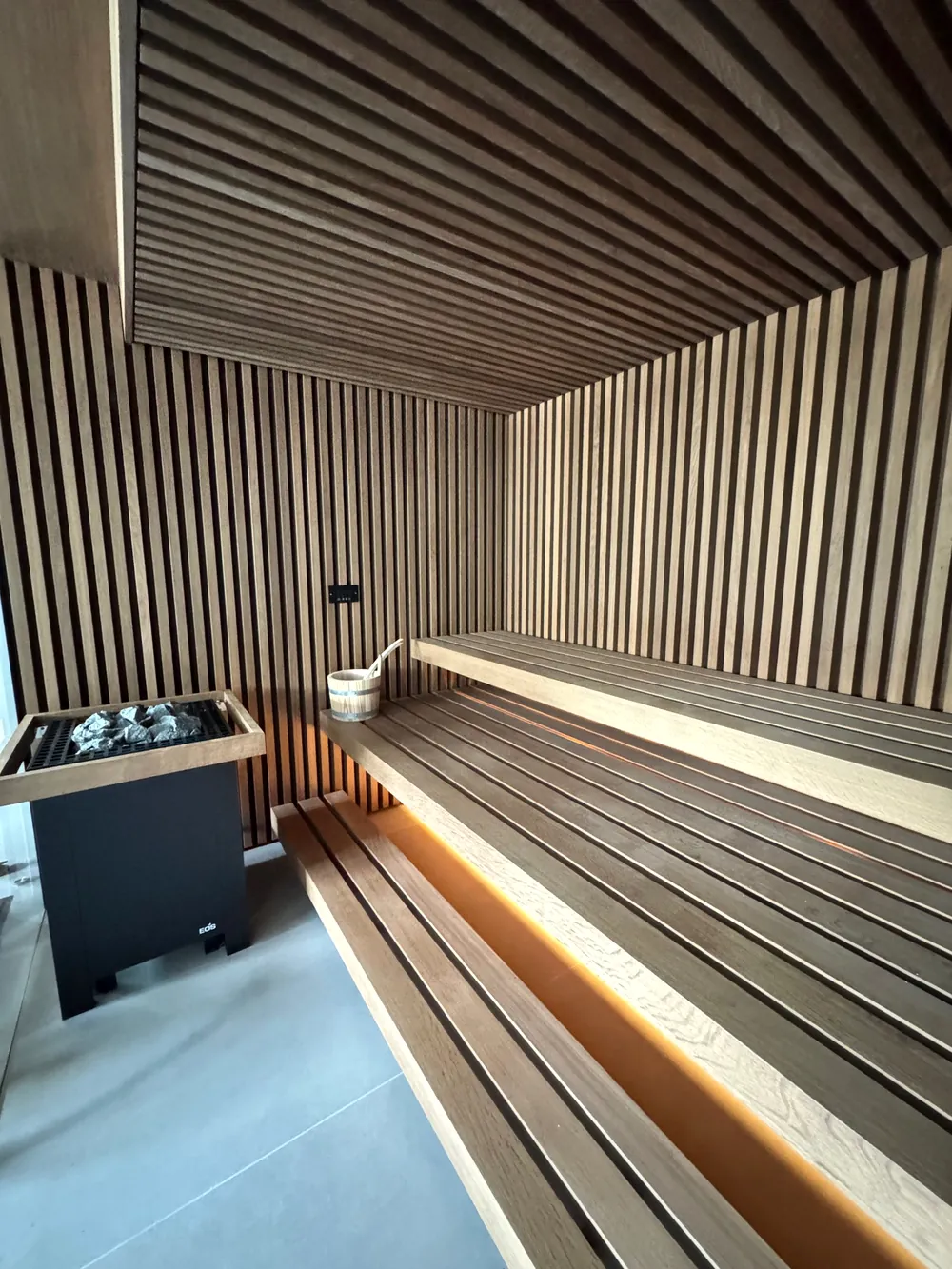 Design-Sauna mit Holzlamellen an Wand und Decke, EOS-Saunaofen und beleuchteter Liegebank