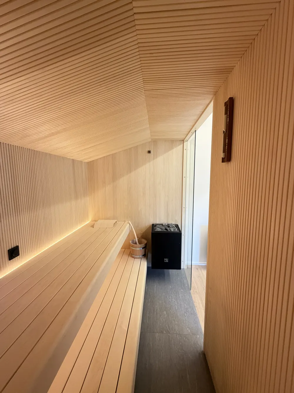 Sauna unter der Dachschräge mit hellem Holz, Liegebank und Saunaofen